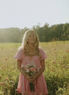 a woman standing in a field holding a bouquet of flowers