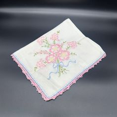 a white handkerchief with pink flowers and blue trimmings on the edge is sitting on a black surface