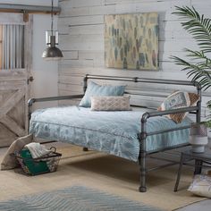 a metal daybed with blue and white bedding in a room next to a plant