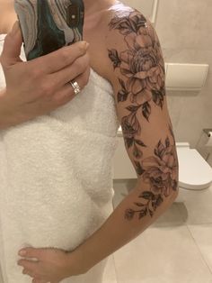 a woman with a flower tattoo on her arm is taking a selfie in the bathroom