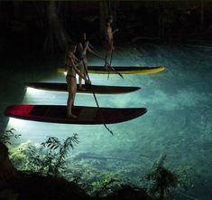 three people standing on paddle boards in the water at night, with lights reflecting off them