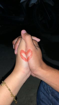 two people holding hands with red lipstick painted on their fingers and the other hand is covering one another's face