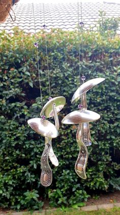 three silver spoons hanging from strings in front of a hedge