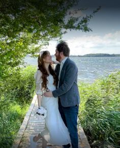 a bride and groom standing on a dock by the water