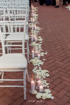 rows of white chairs lined up with flowers and candles on the ground in front of them