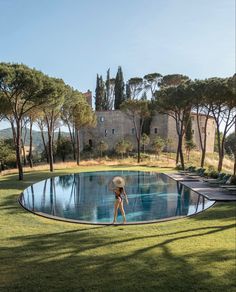 a woman standing in front of a pool surrounded by trees