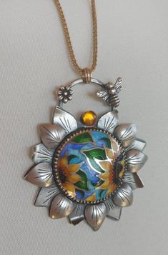 Handmade enamel cloisonne 🌻 Sunflower Pendant (without chain). Can be worn with gold or silver chain.  Check me out on Instagram @anaraandco for shop updates, news, discounts and creative process, please. Handmade with fine and sterling silver, Japanese glass enamel. Adorned with natural stone set in 14K gold bezel, 3 jump rings made out of 14K gold to thread a chain or cord. Gold chain on pictures is not included.  🌻Approximate size 2 x 2.25 in including bail.  🌻Sterling silver, fine silver, 14K gold 🌻Hand sawn and sculpted leaves around enameled center.  🌻 Sterling silver flower and bee on the bail 🌻 Handmade.  Engraved, enameled, hand sawed, soldered, oxidized, tumbled, grinded, polished Thank you for visiting! Sunflower Pendant, Enamel Necklaces, Gold Hand, Sterling Silver Flowers, Gold Hands, Enamel Jewelry, Silver Flowers, Stone Settings, Creative Process