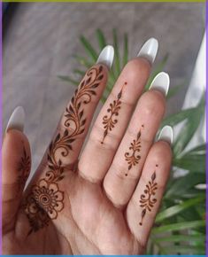 a woman's hand with henna tattoos on it and a plant in the background