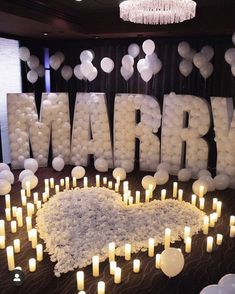 a table topped with lots of candles next to a large sign that says marry surrounded by balloons