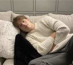 a man laying on top of a white couch next to a black pillow and pillows