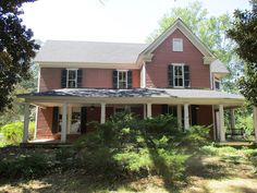 a red house with black shutters on the front and side windows, surrounded by trees