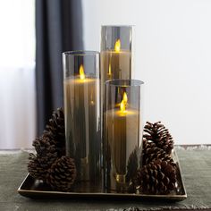 three lit candles on a tray with pine cones