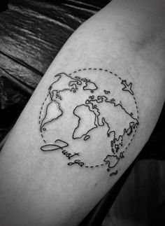 a black and white photo of a world map tattoo on the left arm with an airplane flying around it