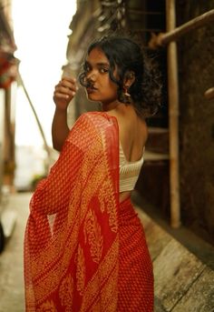 a woman in an orange and red sari is standing on the side of a street