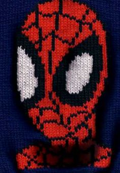 a close up of a knitted spiderman face on a blue sweater with white eyes