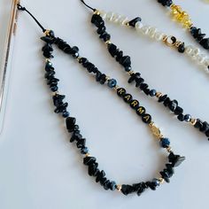 three black and white beaded necklaces sitting on top of a table next to a cell phone