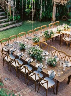 an outdoor dining table set up with place settings and greenery on the tables for dinner