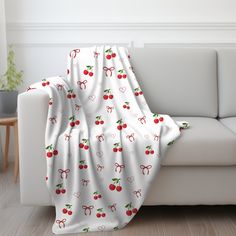 a white couch covered in a cherry print blanket with cherries on the top and bottom