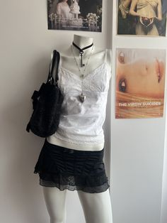 a mannequin wearing a white top and black skirt with pictures on the wall behind it