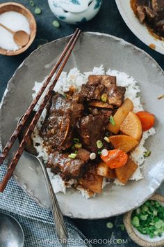 a plate with rice, beef and carrots on it next to chopsticks