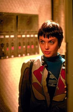 a woman with short hair standing in front of a control panel and looking at the camera