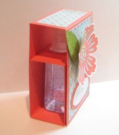 an open box with a flower on the inside and a bottle in the middle, sitting on a table