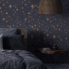 a bed sitting under a lamp next to a night sky wallpaper covered in gold stars