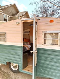 an old trailer with the door open in front of a house and trees behind it