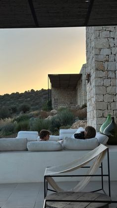 two children laying on couches in front of a stone building with an open patio