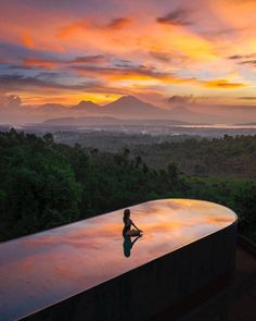 a person sitting on the edge of a swimming pool at sunset with mountains in the background