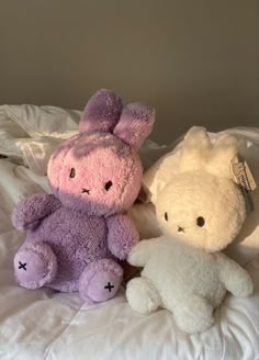 two stuffed animals sitting next to each other on a white sheet covered bedspread