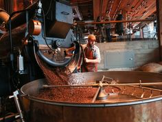 a man standing in front of a large metal pot filled with lots of coffee beans