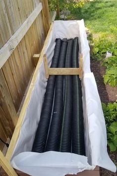 a wooden box filled with black pipes next to a fence and green plants in the back yard