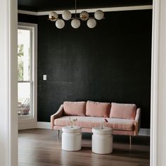 a living room with black walls and pink furniture in the center, along with two white stools