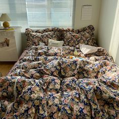 an unmade bed with floral sheets and pillows in a room next to a window