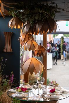 a table with plates and wine glasses on it in front of an outdoor area where people are walking