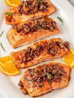 three salmon fillets on a white plate with orange slices