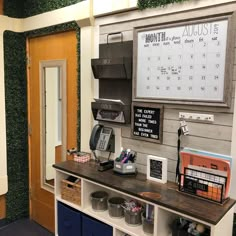 a desk with several items on it in front of a wall mounted calendar and phone