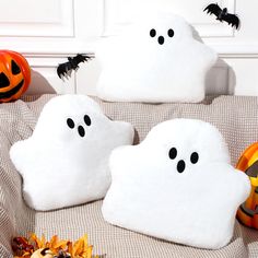 two white pillows with black eyes and ghost faces on them, sitting next to pumpkins