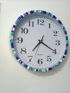 a white clock with blue and green beads on it's face hanging from the wall