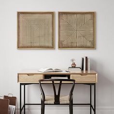 two paintings hang on the wall above a desk with a book and chair in front of it