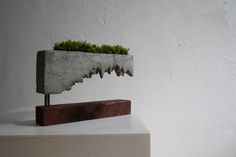 a sculpture with grass growing out of it's sides on top of a block of wood