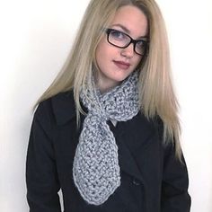 a woman wearing glasses and a knitted scarf is standing in front of a white wall