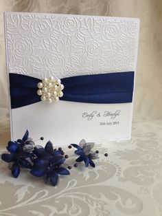 a white card with blue ribbon and pearls on it, next to some purple flowers