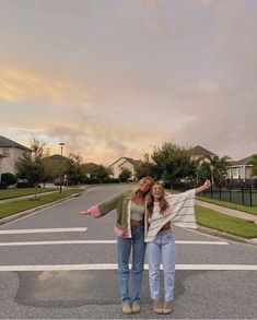 two women standing in the middle of a street with their arms spread out and smiling