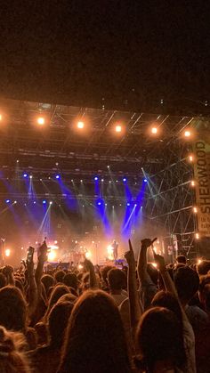 a large group of people at a concert with their hands in the air and lights on