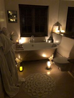 a bath tub sitting next to a white toilet in a room with candles on the floor