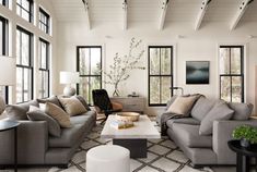 a living room filled with lots of furniture next to tall windows on top of a white floor