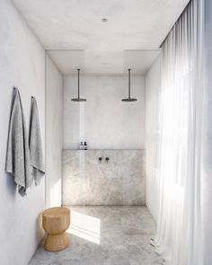 a white bathroom with two towels hanging on the wall and a stool next to it