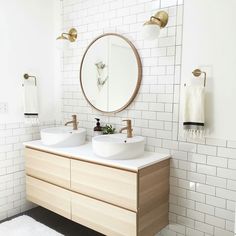 a bathroom with two sinks and a round mirror on the wall next to white tiled walls